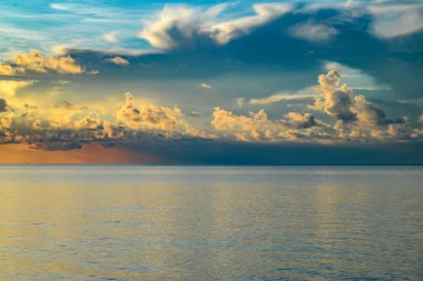Gökyüzü ve bulutların arasından güneş batarken deniz batıyor. Okyanus ve gökyüzü arkaplanı, deniz manzarası.