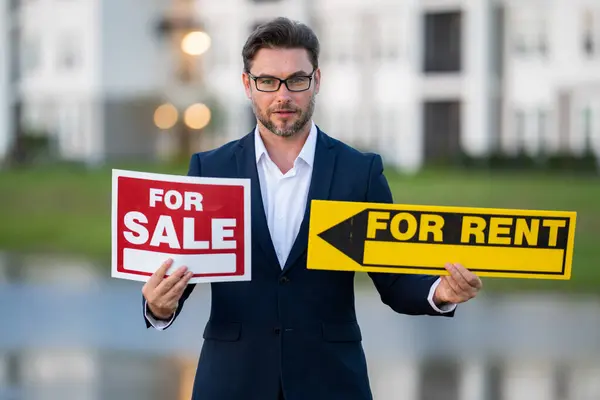 Handsome real estate agent holding banner house for sale. House with land and insurance. Business man real estate agent in business suit presenting the house for sale. Land agent trying to sell house