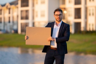 Takım elbiseli adam tabelayı tutuyor, boş kart. Ürününüz için pankart hazır. Mesajını imzala. İşadamı açık havada boş tabela gösteriyor. Boş tahta var. Reklam alanı