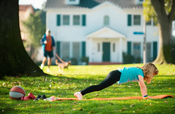 Parkta şınav çeken bir çocuk. Spor, sağlıklı yaşam tarzı, eğitim, açık havada boş zaman. Çocuk yukarı itiyor. Atletik çocuk yeşil çimlerin üzerinde yukarı itiyor. Spor çocukları.