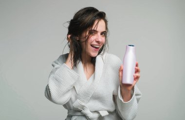 Güzel beyaz kadın ıslak saçlı poz veriyor. Kadın şampuan ve saç kremi tutuyor. Genç kadın reklam ürünleri.