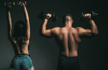Çift halterlerle birlikte egzersiz yapıyor. Çıplak vücutlu kaslı bir adam, arka planda koyu renkli halterleri olan fitness kadını. Seksi, formda bir vücut. Dambılı çift eğitimi