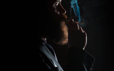 Siyah arka planda sigara içen genç adamın yüzünde koyu bir gölge var. Sigara içen adam