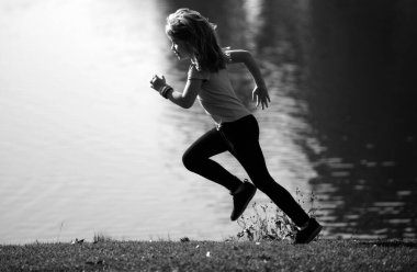 Çocuk parkta çimlerin üzerinde koşuyor ya da göl kenarında koşuyor. Küçük koşucular yaz doğasında dışarıda koşuyorlar. Sportif çocuk parkta koşuyor. Çocuklar için açık hava sporları ve spor. Sabah koşusu