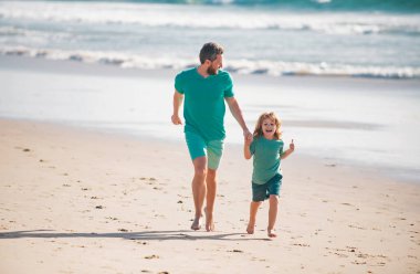 Çocukluk ve ebeveynlik kavramı. Baba oğul yaz plajında koşuyorlar.