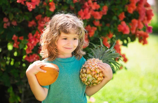 小男孩手里拿着菠萝和椰子 脸上挂着幸福的笑容在院子里 夏季水果 — 图库照片