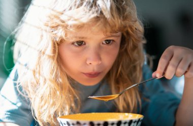 Bulanık arka planda yemek yiyen çocuk. Aç küçük çocuk yemek yiyor. İçeride sebze çorbası içen sevimli küçük okul çocuğu. Çocuklar için ev yemeği