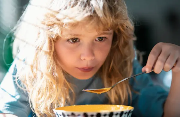 Bulanık arka planda yemek yiyen çocuk. Aç küçük çocuk yemek yiyor. İçeride sebze çorbası içen sevimli küçük okul çocuğu. Çocuklar için ev yemeği