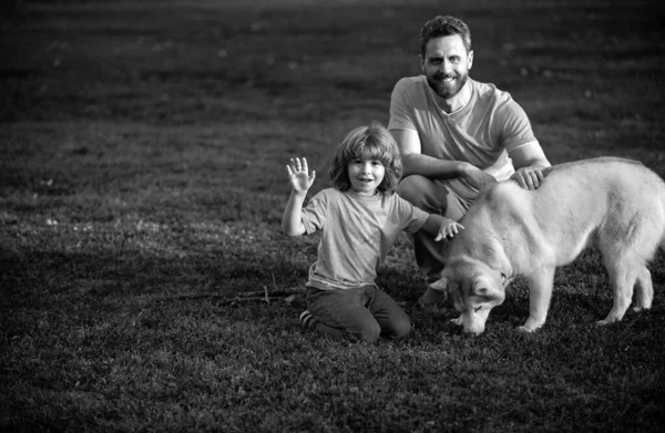 Son and father as family with dog playing together in summer park on grass. Child with her pet friend