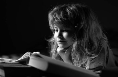 Çocuk masal okuyor, karanlık oda fotoğrafı. Çocuk kitap okuyor. Çocuklar yatma vakti, çocuk yatakta kitap okuyor.