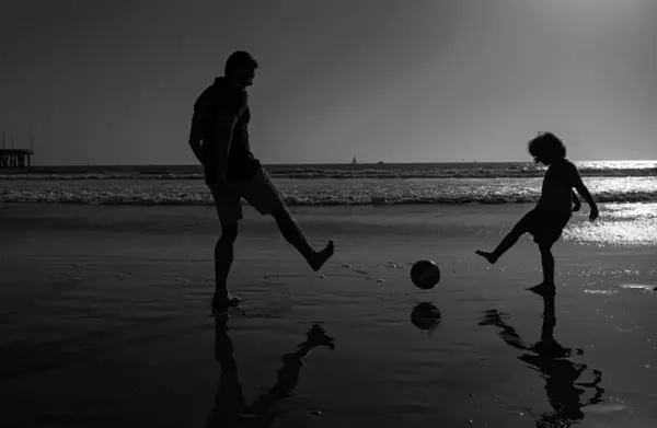 Daddy with kid boy on a summer day. Daddy with kid boy playing on a summer day. Father and son play soccer or football on the beach. Sporty family concept