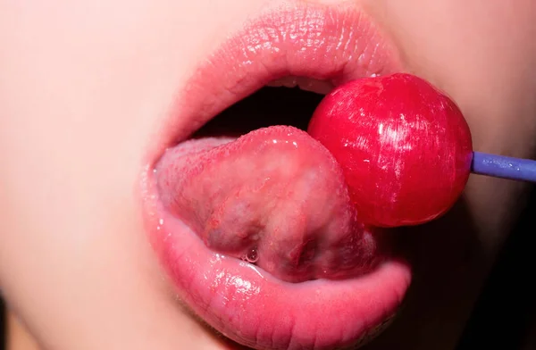 Lollipop in the mouth, close-up. Beautiful girl mouth with lolli pop. Glossy red woman lips with tongue. Mouth lick suck chupa chups