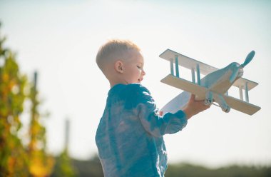 Summer at countryside. Kid dreaming and plays with a toy plane in the park. Dreams of travel. Development, growth, dreams and plans. Imagination and dream concept