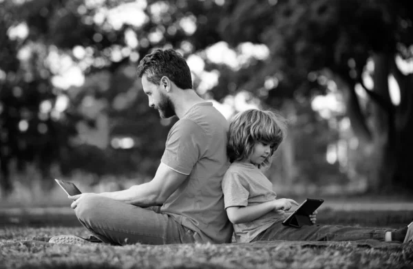 Outdoor distance learning. Father using laptop relax with schooler son holding laptop have fun together. Family with gadgets outside on nature