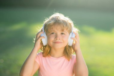 Sevimli küçük çocuk kulaklıkla müzik dinliyor. Çocukluk yaşam tarzı konsepti. Çocuk parkta yaz müziğinin tadını çıkarıyor.