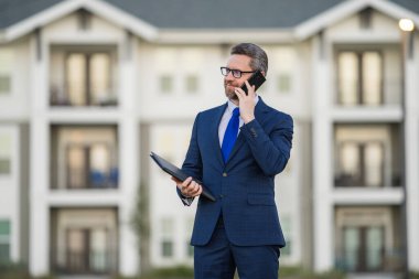 Emlakçı, takım elbiseli iş adamı. Elinde not defteri var ve telefonda konuşuyor. İş adamı. İş adamı komisyoncusu ya da emlakçı. Takım elbiseli bir iş adamı. İş teklifi, satın alma teklifi