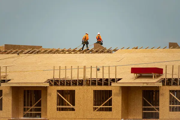 Roofing on roof. Builder roofer install new roof. Construction worker roofing on a large roof apartment building development. Roofer carpenter working on roof structure construction site