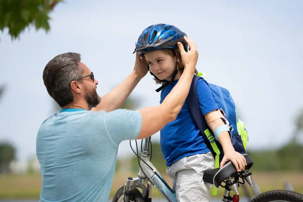 Little kid learning to ride bicycle with father in park. Father teaching son cycling. Father and son learning to ride a bicycle at Fathers day. Father helping his son to wear a cycling helmet