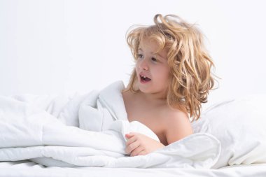 Büyük yatakta yatan küçük bir çocuğun portresi. Mutlu çocukların evde iyi vakit geçirmesi kavramı. Çocuk yatakta uyandı.