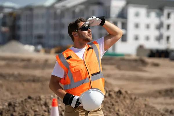 Tired worker. Worker man on the building construction. Construction site worker in helmet work outdoors. Builder worker working on construction site. Construction site worker outdoor portrait