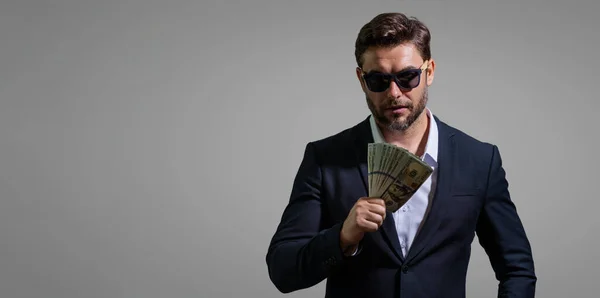 Business man hold money on gray studio isolated background. Rich man in suit with money dollar bills. Businessman with dollar banknotes. Rich millionaire in suit holding money. Banner copy space