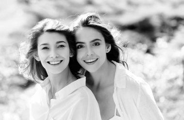 Birlikte duran ve yeşil bahar arka planında kameraya bakan iki neşeli genç kadının portresi.