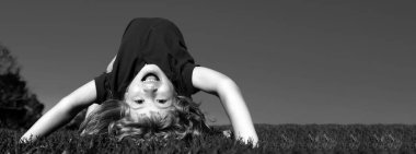 Bahar çocukları portresi olan pankart. Mutlu çocuk yeşil çimenlerde baş aşağı oynuyor. Baharın bahçesinde komik bir çocuk. Çocuk günü. Mutlu tasasız çocukluk konsepti