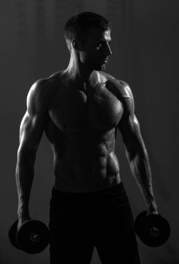 Sportif gövde, dambılı adam. Dambılı bir sporcunun portresi. Stüdyoda kaslı, gömleksiz bir adam var.