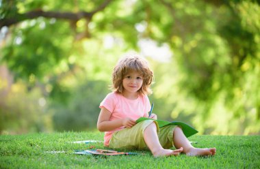 Parkta okuyan sevimli küçük bir öğrenci ve açık havada çocukların eğitimi için gülümsüyor