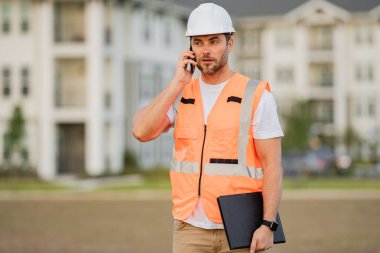 İnşaatçı telefonu kullanıyor. Miğferli inşaat işçisi yeni bir ev inşa etti. Mühendis, inşaat üniforması ve başlık giyiyor. Foreman açık hava portresi. 40 'lı yılların işçisi, bin yıllık İspanyol mühendis inşaatçısı.