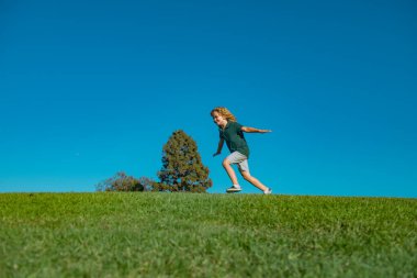 Yeşil çimenlerde koşan gülümseyen bir çocuğun portresi. Doğanın tadını çıkaran sevimli bir çocuk. Yaz parkında oynayan kaygısız sağlıklı bir çocuk. Sağlıklı çocuklar açık hava yaşam tarzı konsepti