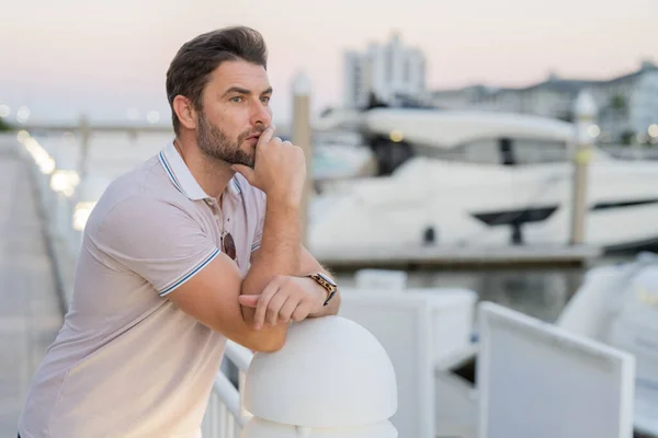 Rich business man dreaming and thinking near the yacht. Fashion male posing on the street background. Urban style. Young man walk through the city. Wealthy businessman posing next to office building