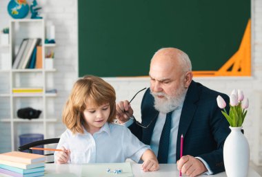 Okuldaki mutlu çocuk. Eski kıdemli öğretmen yazmaya yardım eder. Eğitim, öğretmenlik, ilkokul