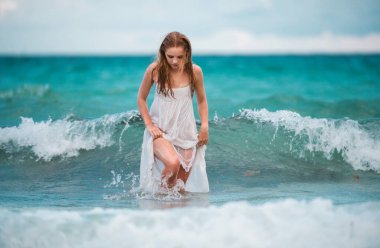 Dalgalar denizindeki genç seksi kadın. Yaz plajı şehvetli kızı. Beyaz elbiseli kız tropik plaj tatilinde.