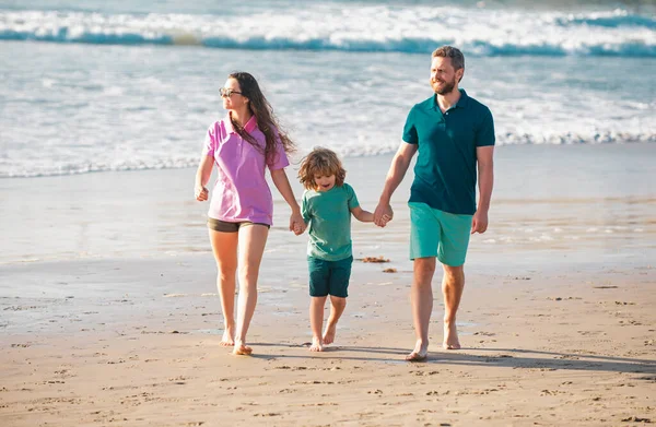 Family walking on beach. Mother father and child son spending time together. Family summer vacation. Parent dad mom walking with son holds hand barefoot on sea