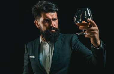 Elit alkolün yok sayıltıcısı. Siyah takım elbiseli, konyak lı kendine güvenen sakallı adam. Sakallı adam brendi bardağı tutar