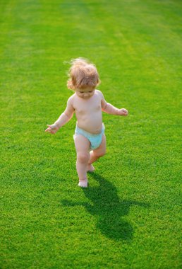 İlk adım. Parlak bir bahar gününde parkta yürüyen küçük bir çocuk. Yeşil çimlerin üzerinde duran bebek çıplak bacakları. Çocuk gelişimi