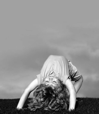 Yazlık parktaki çimlerde baş aşağı oynayan mutlu çocukların portreleri. Doğayla oynayan çocuklar. Boşluğu mavi gökyüzünde kopyala.