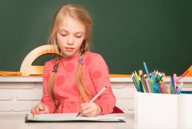 Okul öğrencisi çalışmak için kitaptan notlar alıyor. Okulda tahtaya yakın bir okul çocuğu.