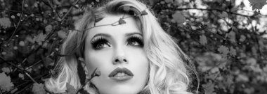 Bahar kadını pankarta karşı. Çiçek tarlasında parlak makyajlı bir kadın. Profesyonel makyajlı sarışın kız ve fevkalade fantezi saç stili açık havada poz veren taze çiçekler.