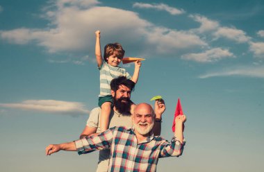İnsanların nesli ve büyüme aşamaları. Kağıt uçak ile çocuk pilot havacı seyahat hayalleri. Baba ve dedesi ile genç çocuk mavi gökyüzü arka plan üzerinde parkta birlikte zevk