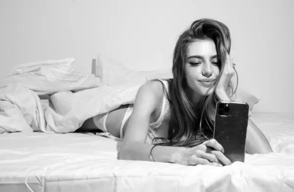Woman in bed checking social apps with smartphone. Sexy girl making video call, lying on bed in the morning