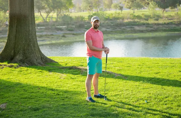 Golf sopası, sıcak bir akşamda bir golf sahasındaki çimlerin üzerinde duran bir adam.