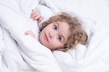 Child wakes up from sleep in bed. Kid wakes up in the morning in the bedroom