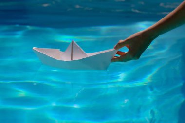 Elle kağıt tekne. Turizm ve seyahat, seyahat hayalleri tatil tatili, yelkenli macerası. Mavi su yüzeyinde yüzen kağıt tekne.