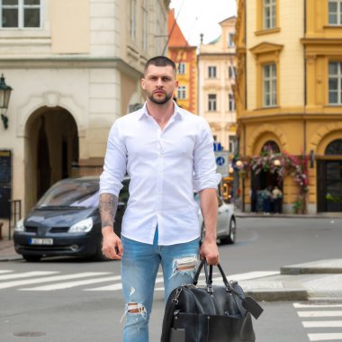 İş gezisindeki yakışıklı genç adam bavuluyla sokakta yürüyor. Gezgin iş adamı.