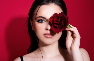 Mavi gözlü ve kırmızı güllü esmer kadın. Çiçekleri olan güzel bir kız. Temiz ciltli ve parlak makyajlı güzel bir kadının yakından çekilmiş yüzü.