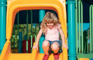 Kaydırağın üzerinde oynayan mutlu çocuk. Çocuk parkında oynarken sevimli küçük çocuk komikliği. Yaz çocukları