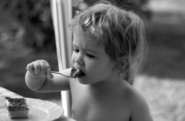 Bebek pasta yiyor. Komik şirin çocuk tatlı kek yiyor. Çocuk piknikte kaşıkla tatlı yiyor.