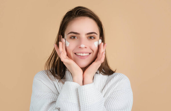 Beautiful girl model with natural makeup applying moisturizer cream on her pretty face